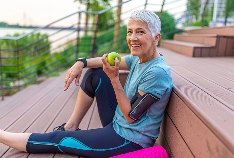 Woman holding an apple, representing a strong and healthy smile with dental implants services at Deluxe Dental in Miami, Kendall, and Medley.