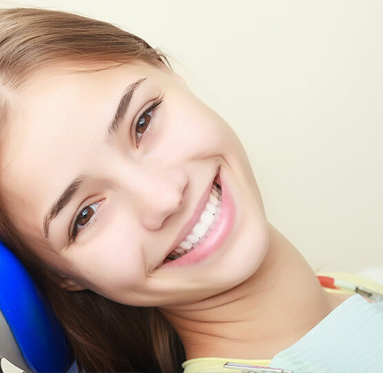 Close-up of a beautiful young woman in a dental chair, smiling confidently and showcasing her bright smile, representing smile design treatment at Deluxe Dental in Miami, Kendall, and Medley.