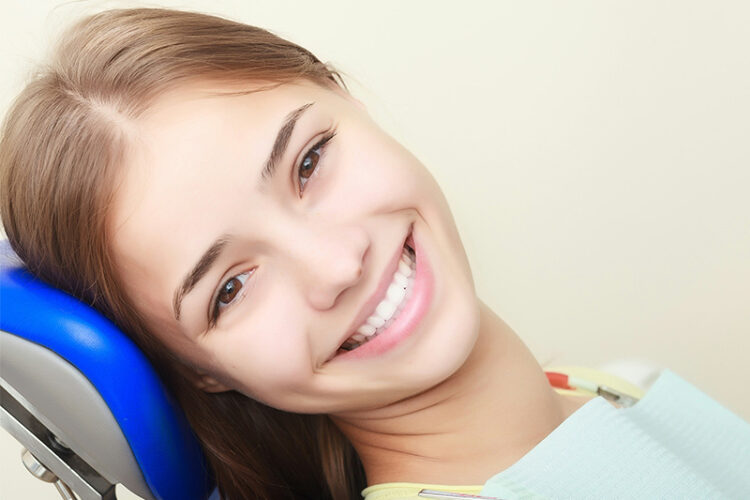 Close-up of a beautiful young woman in a dental chair, smiling confidently and showcasing her bright smile, representing smile design treatment at Deluxe Dental in Miami, Kendall, and Medley.