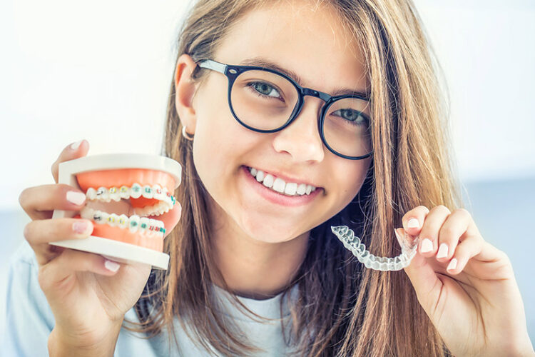 Teen holding a braces model and a clear aligner model, representing orthodontic treatment options available at Deluxe Dental in Miami, Kendall, and Medley.