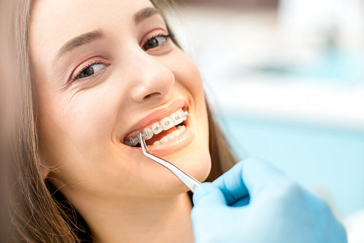Patient in the dental chair smiling while a dentist adjusts their braces treatment, representing orthodontic care at Deluxe Dental in Miami.