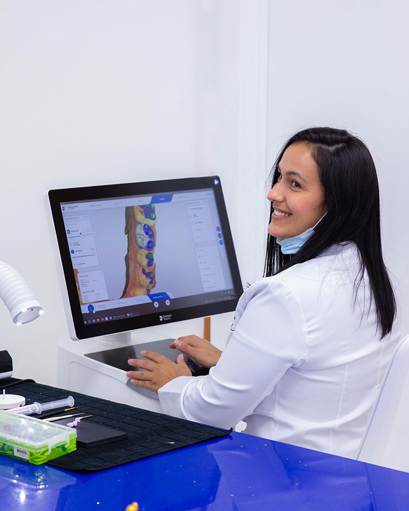 Dental lab technician Jany smiling while designing a dental restoration on her computer at Deluxe Dental, using advanced technology and digital scanning